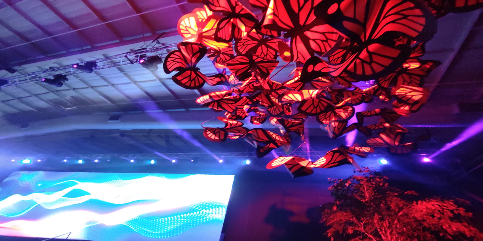 A swarm of red paper butterflies hanging over a stage with an LED wall