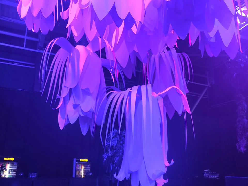 Giant white paper flowers hanging from a venue ceiling, lit in pink and violet