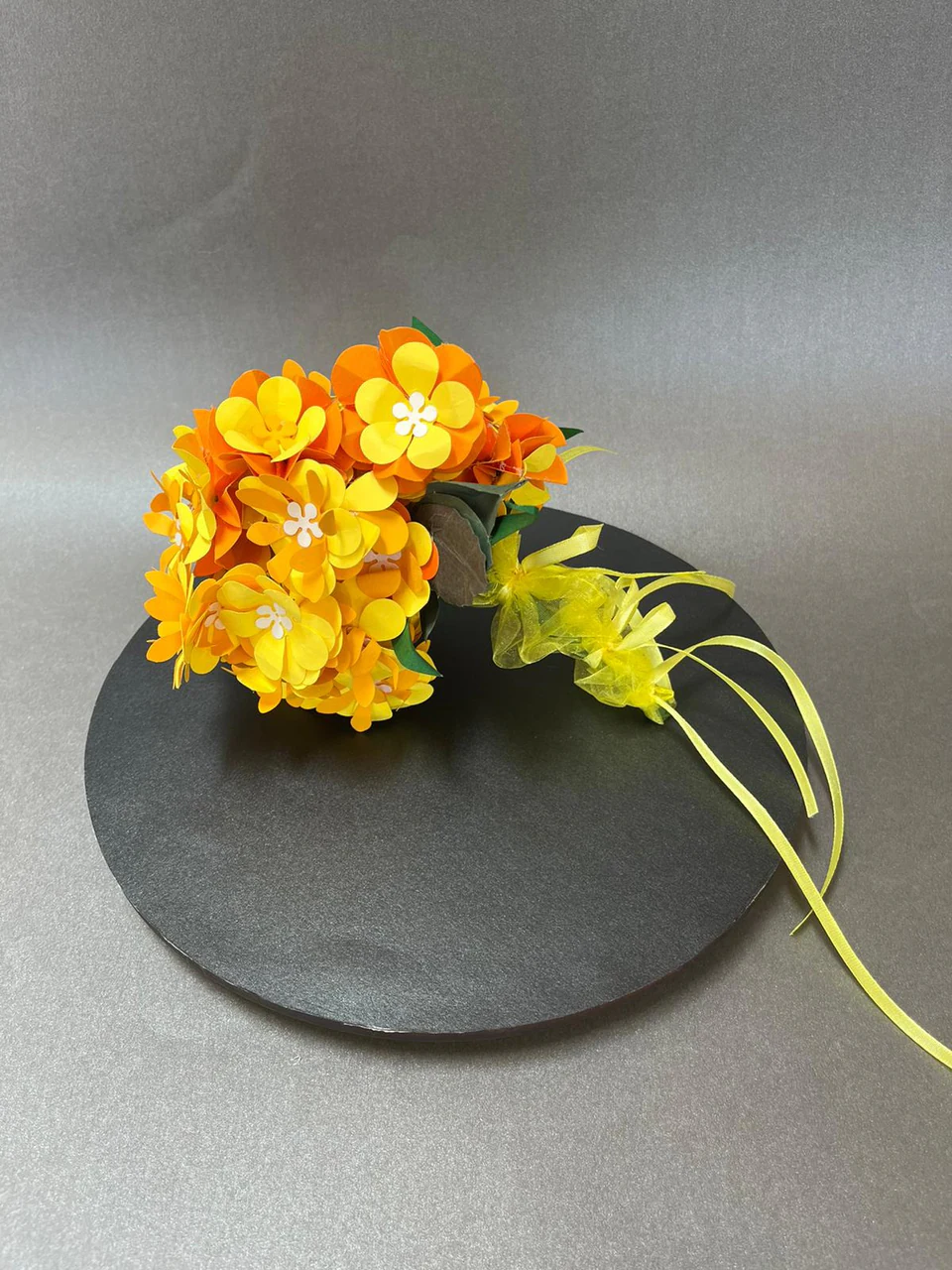 A cluster of yellow and orange paper blossoms with a trailing ribbon
