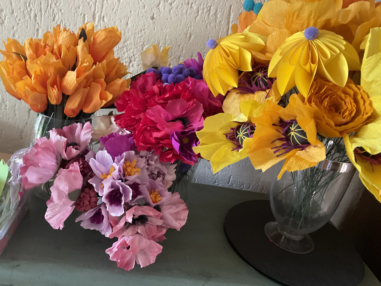Crepe paper poppies, carnations and anemones in glass vases on a counter