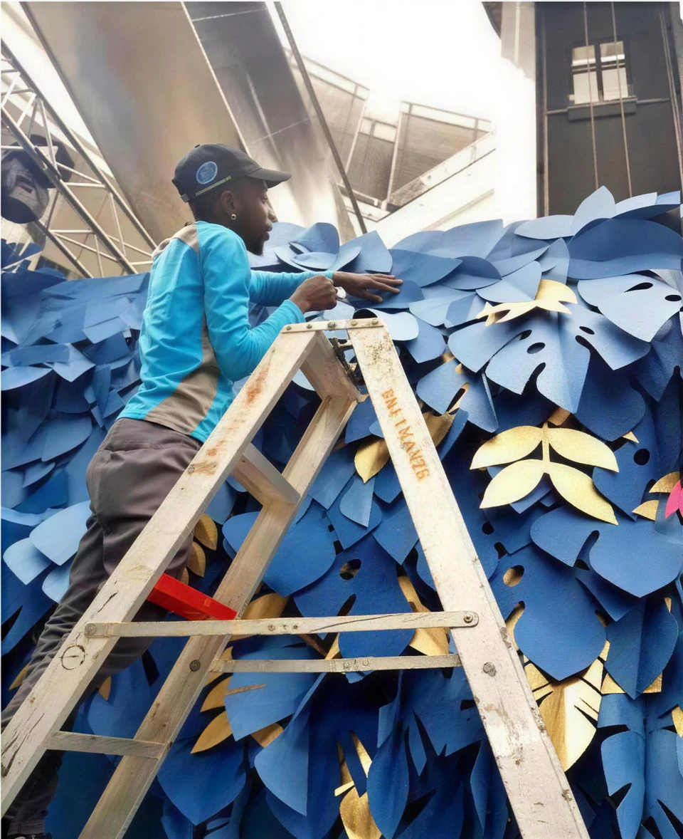 An installer on a ladder fixing blue and gold paper leaves to a wall